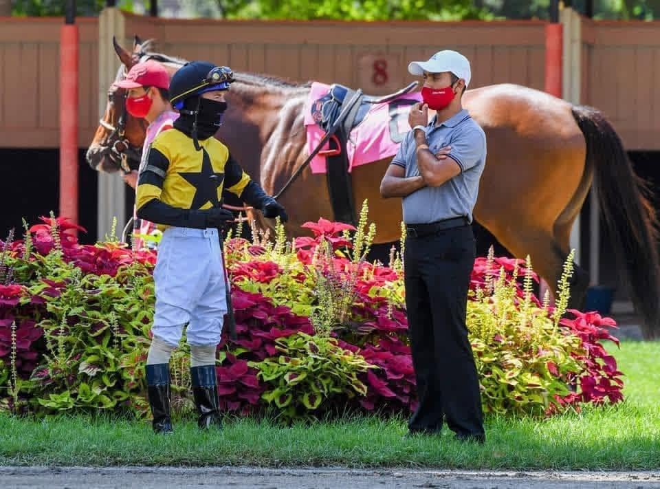 A racehorse, jockey and team beside a flower-lined paddock; photo shared by Yoni Orantes